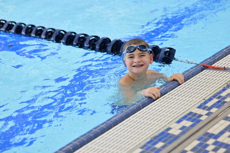 A young swimmer smiles poolside during the Aquatics program practice meet