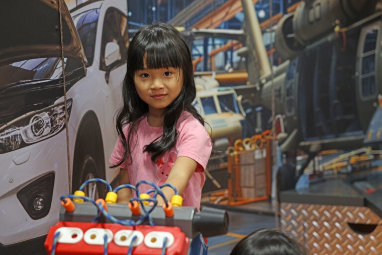 Elementary aged child smiling while working with toy engine machine with mechanical background.