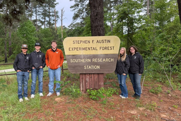 A group of five people standing in front of a sign for the Stephen F. Austin Experimental Forest Southern Research Station. The background features trees and greenery.