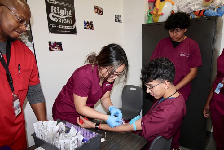 Students work on their phlebotomy skills as instructor watches on